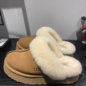 Bruna tofflor från UGG - Mysiga bruna tofflor från UGG med mjuk päls i beige. De är helt oanvända, har även boxen kvar ( skulle säga att de är lite små i storleken, jag har vanligtvis 38 och dessa passar mig)