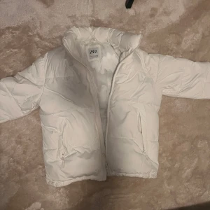Vit pufferjacka från Zara - Säljer en snygg vit pufferjacka från Zara. Jackan har en dragkedja framtill och är långärmad. Perfekt för kyligare dagar med sin quiltade design som håller värmen.har bara en rosa fläck men kan säkert gå bort med tvättning