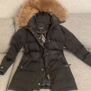 Svart dunjacka från Hollies - Snygg svart dunjacka från Hollies med pälskantad huva. Jackan har dragkedja och knappar framtill samt praktiska fickor med dragkedja. Perfekt för kalla vinterdagar. Saknas en knapp på baksidan. Finns knappar att sy fast som tillkom när jag köpte jackan. Köpte jackan för 5000 på rabatt. Men säljer för 3500kr kan diskuteras🫶🏽