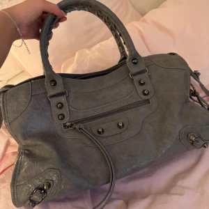 Grå väska med dragkedja - Supersnygg grå väska med dragkedja, flätat handtag och nitdetaljer. Kommer även med en avtagbar spegel. 