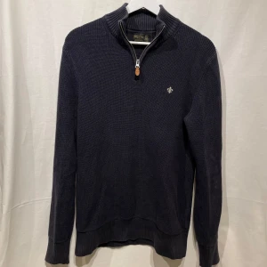 Mörkblå stickad tröja från Morris - Snygg mörkblå stickad tröja från Morris half-zip och broderad märke på bröstet. Perfekt för kyligare dagar eller sena sommarkvällar, modellen är 180cm