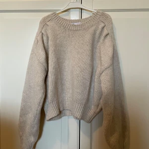 Beige stickad tröja - Mysig beige stickad tröja med rund hals och långa ärmar. Perfekt för kyliga dagar med sin mjuka och bekväma passform. Ribbstickade muddar vid ärmslut och nederkant ger en stilren look.