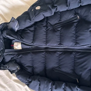 Marinblå montgenevre från Moncler - Snygg marinblå dunjacka från Moncler med dragkedja och praktiska fickor. Jackan har en quiltad design och en hög krage för extra värme. Perfekt för kyliga dagar. Säljer för att den inte kommit till användning, ny skick utan kvitto och Scan funkar