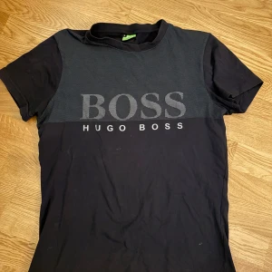 Svart t-shirt från Hugo Boss - Snygg svart t-shirt från Hugo Boss med stort BOSS-tryck över bröstet. Den har en klassisk rund hals och korta ärmar, perfekt för en stilren look. Materialet känns mjukt och bekvämt.