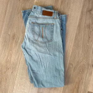 Ljusblå jeans från Fornarina - Säljer ett par ljusblå jeans från Fornarina med klassisk femficksdesign och orange sömmar. Jeansen har en straight passform och är perfekta för en avslappnad stil.