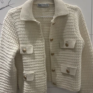 Vit stickad kofta från Zara - Snygg vit stickad kofta från Zara med guldknappar och två fickor framtill. Jackan har en klassisk krage 