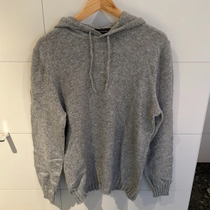 Grå stickad hoodie från Dressmann - Säljer en grå stickad hoodie från Dressmann. Den har en bekväm passform och är perfekt för kyliga dagar.