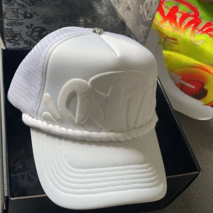 Syna world keps - Snygg vit syna world keps med broderad text och nätpaneler för ventilation. Kepsen har en dekorativ snodd framtill och justerbar passform baktill. Perfekt för en stilren look. Kepsen finns inte längre så den är väldigt sällsynt.