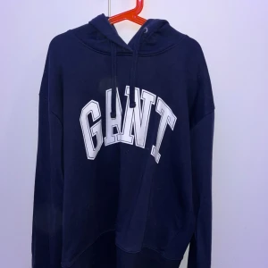 Mörkblå hoodie från GANT - Säljer en snygg mörkblå hoodie från GANT med stor logga framtill. Den har en klassisk huva med dragsko och långa ärmar.