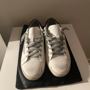 vita skor med stjärn detaljer! - Snygga vita sneakers med grå snörning och en stjärndetalj på sidan. Skorna har en klassisk design med en robust sula och mörkblå detaljer vid hälen. Storlek 41, fast känns som en 39-40