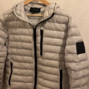 Ljus Grå dunjacka från Peak Performance - Snygg och stilren grå dunjacka från Peak Performance. Jackan har en dragkedja framtill och praktiska fickor med dragkedjor. Perfekt för kyligare dagar med sin quiltade design och långa ärmar. Passar M eventuellt S ✅