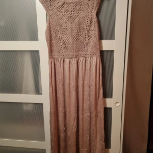 Långklänning från H&M - Elegant långklänning från H&M med vackra spetsdetaljer på överdelen. Klänningen har en rund hals och är ärmlös, vilket ger en stilren look. Perfekt för speciella tillfällen. Ny, aldrig använd. 