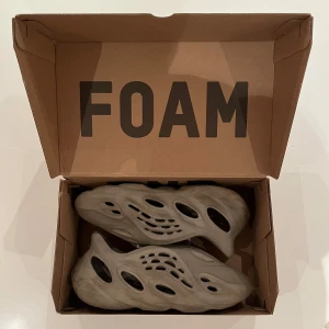 Beige Adidas Yeezy Foam Runner - Säljer ett par beige Adidas Yeezy Foam Runner med unik design och hålmönster för ventilation. Perfekta för en avslappnad stil. Nypris ca 2000kr