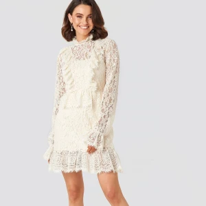 Vit spetsklänning med volanger från NA-KD - Elegant vit spetsklänning med långa ärmar och vackra volangdetaljer. Aldrig använd. 