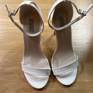 Vita sandaler med klack från NLY Shoes - Eleganta vita sandaler med smal klack och justerbart spänne runt ankeln från NLY Shoes. Perfekta för en stilren look. Klack ca 11 cm