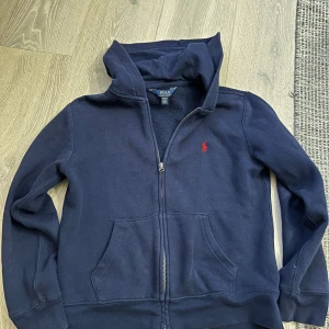 Mörkblå ziphoodie från Ralph Lauren - Säljer en stilren mörkblå ziphoodie från Ralph Lauren med dragkedja. Den har storlek M (10-12 år) i juniorstorlek och XS i herr. Nypris 1195 kr. Skicket är 8/10.