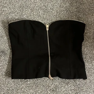 Svart tubtopp från Zara - Snygg svart tubtopp från Zara med dragkedja framtill. Perfekt för en stilren look. Tillverkad i ett mjukt material som sitter bekvämt. Är vanligtvis en s💕(användt en gång)