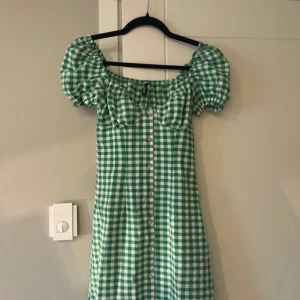 Grön och vit rutig klänning  - Charmig grön och vit rutig klänning med puffiga kortärmar och knappar framtill. 