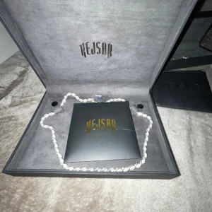 Smycken från Kejsar - Elegant smyckeset från Kejsar med ett armband och ett halsband. Armbandet har röda fyrklöverformade detaljer och halsbandet har en blå droppformad hängande sten. Perfekt för att ge en touch av färg och stil.