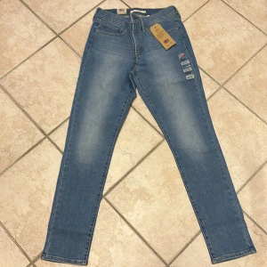 Levi's 311 Shaping Skinny Jeans - Snygga Levi's 311 Shaping Skinny jeans i en ljus blå färg. Dessa jeans har en midwaist passform och är designade för att forma och slimma figuren. Perfekta för en stilren look. Helt NYA!