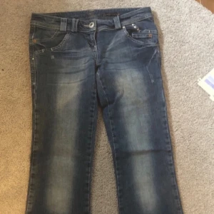 Blå jeans med detaljer - Säljer ett par snygga blå lågmidjade jeans med slitna detaljer och dekorativa bakfickor. Passar nån runt 160-165