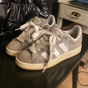 Grå Adidas Campus - Snygga grå Adidas sneakers med vita detaljer och klassiska ränder. Skorna har en gummisula och är tillverkade i mocka. Säljer pga för stora och glappar när jag går. Köpa för 1’450 och säljer för 850. Skulle säga att dom är i rätt bra skick och har inte haft så länge. Tvättar innan jag postar såklart 😊
