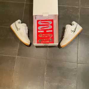 Nike Air Force 1 Travis Scott - Säljer ett par vita Nike Air Force 1 Travis Scott med silverfärgade detaljer och gummisula. Skorna har en unik design med avtagbara swooshes och dekorativa element på snörningen. Perfekta för sneaker-entusiaster! Även använd en gång då dom blev smutsiga på framsidan men är enkelt att tvätta! Säljer dom billigt eftersom jag vill helst bli av med dom för det inte är min stil.