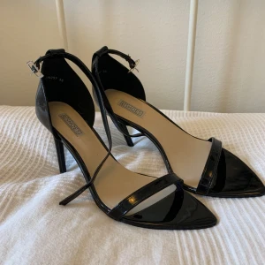 Svarta klackskor  - Jättefina svarta klackar från Nelly. Stl 38 med justerbart band runt ankeln. Jättegott skick. 