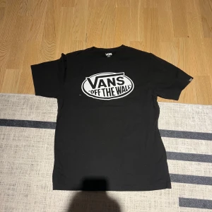 Svart t-shirt från Vans - Snygg svart t-shirt från Vans med det klassiska 'Off The Wall'-trycket i vitt på framsidan. Tillverkad i 100% bomull för en bekväm passform. Perfekt för en avslappnad stil.