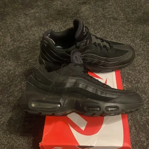 Svarta Nike Air Max 95 - Säljer ett par svarta Nike Air Max med klassisk design och synlig luftdämpning i sulan. Skorna har snörning och är perfekta för en sportig look. Skorna är smått slitna där bak. Nypris:2300