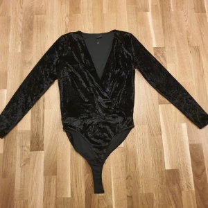 Svart body i sammet  - Helt ny i sin etikett!!  Snygg svart body i mjuk sammet från Gina Tricot. Den har en omlott-design med v-ringning och långa ärmar. Perfekt för en elegant look. Stl.M