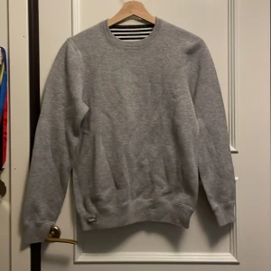 Lacoste tröja - Säljer en  fin Lacoste sweatshirt. Använd ett fåtal gånger,  i väldigt fint skick. Storleken på den är S men skulle säga att den även passar XS. Går att ha den helgrå eller så kan man vända på den och ha svartvit randig. Nypris 1200kr, mitt pris 325