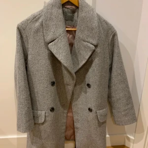 Grå kappa från oanvänd  - Säljer en stilren grå kappa från Mango. Den har en klassisk design elegant touch till vilken outfit som helst. Kappan har långa ärmar och två fickor framtill. Super