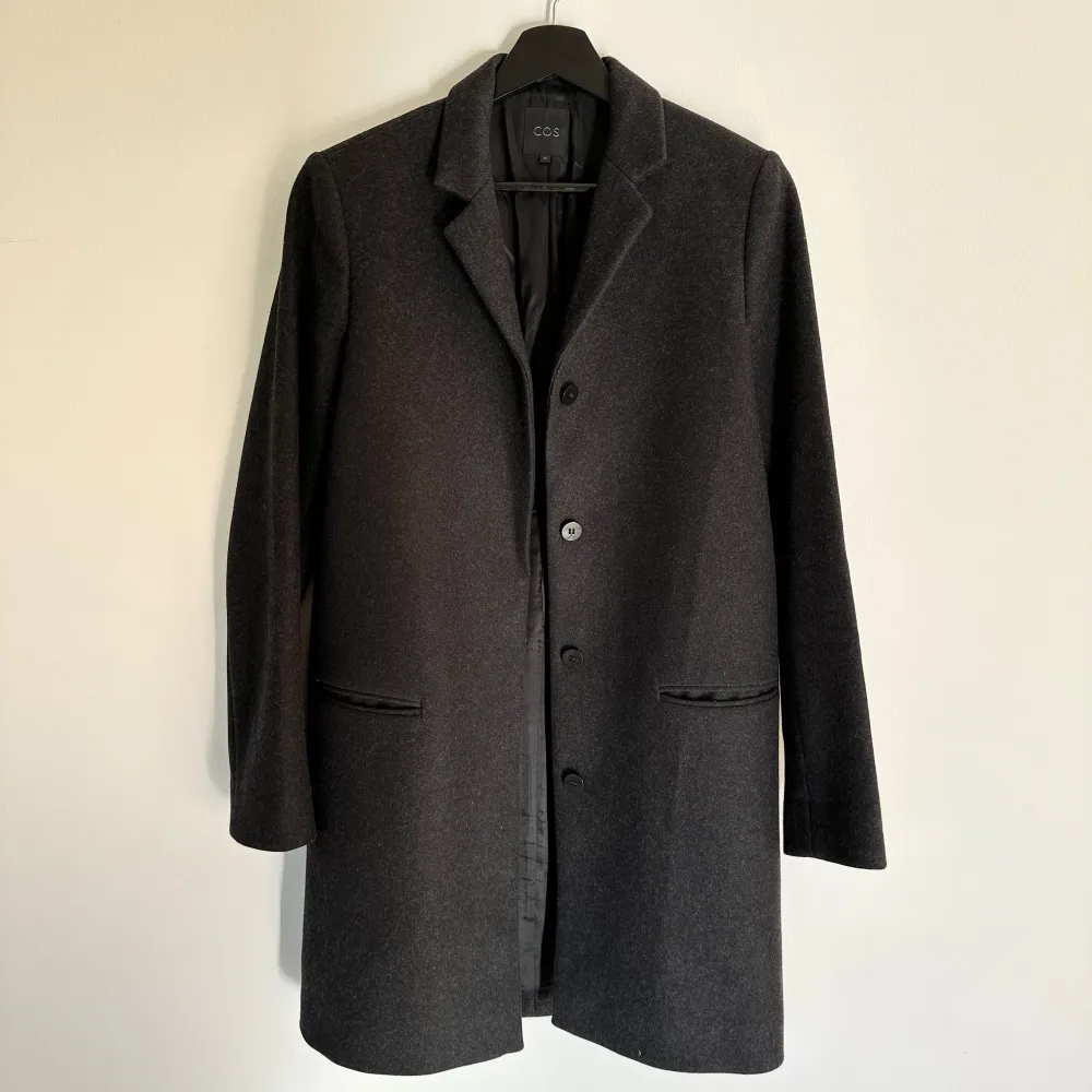 En mörkgrå kappa i rak och lite tunnare modell. Mycket stilren och perfekt som höstkappa. 70% ull, 20% polyamid, 10% cashmere.  Mycket bra skick, som ny då den knappt är använd.  . Jackor.