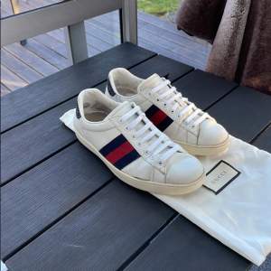 Säljer ett par snygga vita sneakers från Gucci. De har de klassiska ränderna i blått och rött på sidan och en cool detalj i svart på hälen. Skorna är i bra skick med lite slitage på sulorna. Ny pris 8500 kr mitt pris 1599