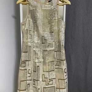 Beige mönstrad klänning från Raxevsky - Säljer en superfin beige klänning från Raxevsky i storlek S. Den har ett unikt geometriskt mönster som verkligen sticker ut. Klänningen är ärmlös och har en rak passform som är både bekväm och stilren. Perfekt för både vardag och fest!