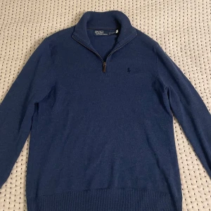 Blå tröja från Polo Ralph Lauren - Säljer en snygg blå ull tröja från Polo Ralph Lauren. Den har en dragkedja vid halsen och är perfekt för både vardag och lite finare tillfällen. Tröjan är i nästan nyskick. 100% merinoull. Perfekt för höst och vinter!