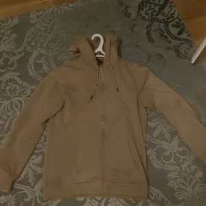 Beige hoodie med dragkedja - Säljer en stilren beige hoodie med dragkedja och justerbar huva. Perfekt för kyliga dagar och passar till det mesta. Tillverkad i Turkiet.