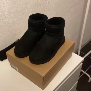 Uggs - Säljer ett par svarta UGGs i mocka. De är perfekta för kyligare väder och har en bekväm passform. Sulan är mönstrad för extra grepp. Enkla att matcha med olika outfits. Storleken är 40 men passar typ 40,5-41. Dom är använda i 2 veckor Max så dom är i princip nya
