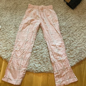 Rosa pyjamas byxor från Gina Tricot i storlek 134/140 - Säljer ett par mjuka och bekväma rosa pyjamas byxor från Gina Tricot med rutigt mönster. Byxorna har en elastisk midja för extra komfort. Perfekta för en avslappnad stil.