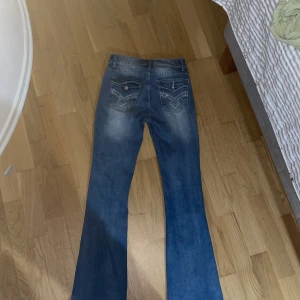 Blå bootcut jeans med broderade detaljer - Snygga blå bootcut jeans med broderade detaljer på bakfickorna. Perfekta för en avslappnad stil med en touch av elegans. Passar bra till både t-shirt och blus. De är andvända men funkar som vanligt 