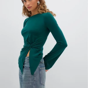 Grön långärmad topp med knytdetalj - Snygg grön långärmad topp med en unik knytdetalj framtill. Perfekt för att ge en stilren touch till din outfit. Passar bra till jeans eller kjol. Oanvänd och köpt för 299kr
