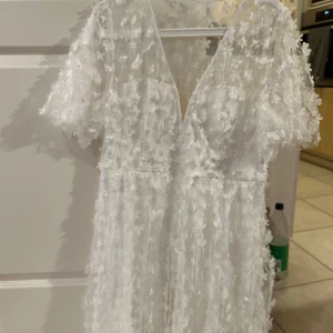 Vit blommig klänning - Säljer en vacker vit klänning med blommigt mönster och v-ringad design. Klänningen har korta ärmar och en luftig passform, perfekt för sommarens festligheter. Använd endast 1 gång. Perfekt till studenten. Nypris: 999