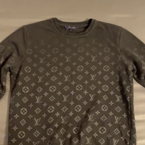 Svart tröja från Louis Vuitton - Säljer en stilren grå tröja från Louis Vuitton med det ikoniska monogrammönstret. Tröjan har långa ärmar och en rund halsringning, perfekt för en trendig look.