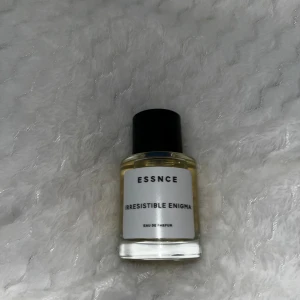 Essnce Irresistible Enigma Eau de Parfum - Säljer en flaska Essnce Irresistible Enigma Eau de Parfum. Flaskan är genomskinlig med en svart kork och har en stilren etikett. Perfekt för den som söker en unik doftupplevelse.