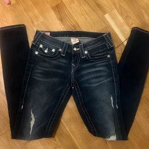 True religion jeans - Snygga true religion jeans med slitningar och kontrastsömmar. De har en femficksdesign och dekorativa bakfickor med knappar. Modellen är skinny 