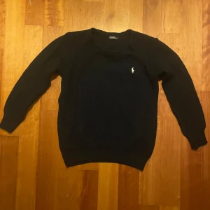 Ralph lauren tröja - Säljer en stilren svart/mörkblå stickad tröja från Ralph Lauren med bruna armbågslappar. Tröjan har en vit liten broderad logga på bröstet och långa ärmar. Perfekt för kyliga dagar!