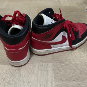 Nike Air Jordans i rött, svart och vitt - Säljer ett par klassiska Nike Air Jordans i rött, svart och vitt. Skorna har en hög design med snörning och den ikoniska Air Jordan-loggan på sidan. Perfekta för dig som vill ha en stilren och sportig look. sparsamt använda