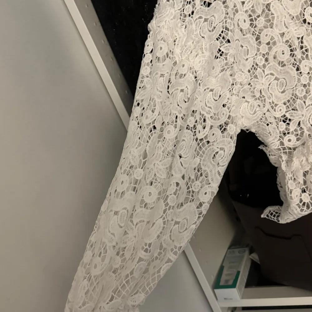Elegant vit spetstopp med vackra detaljer och volanger. Toppen har långärmade ärmar en design som passar perfekt för speciella tillfällen.. Puserot.