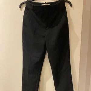 Svarta kostymbyxor - Eleganta svarta kostymbyxor med en klassisk design. Byxorna har en rak passform och är utrustade med diskreta fickor baktill samt sprunn nertill på byxbenens insida. Perfekta för en stilren look.